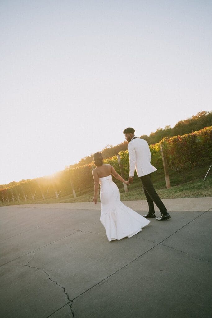 Bride and groom walking through Morais Vineyards vineyard at sunset