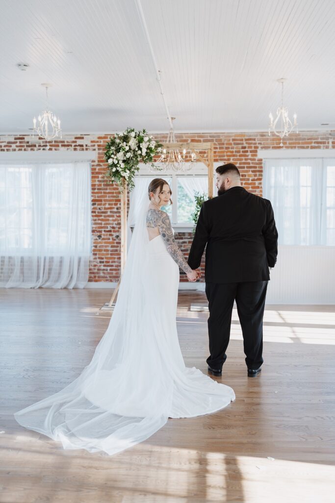 Bride looking over her shoulder while standing with the groom inside The Woolen Mill.